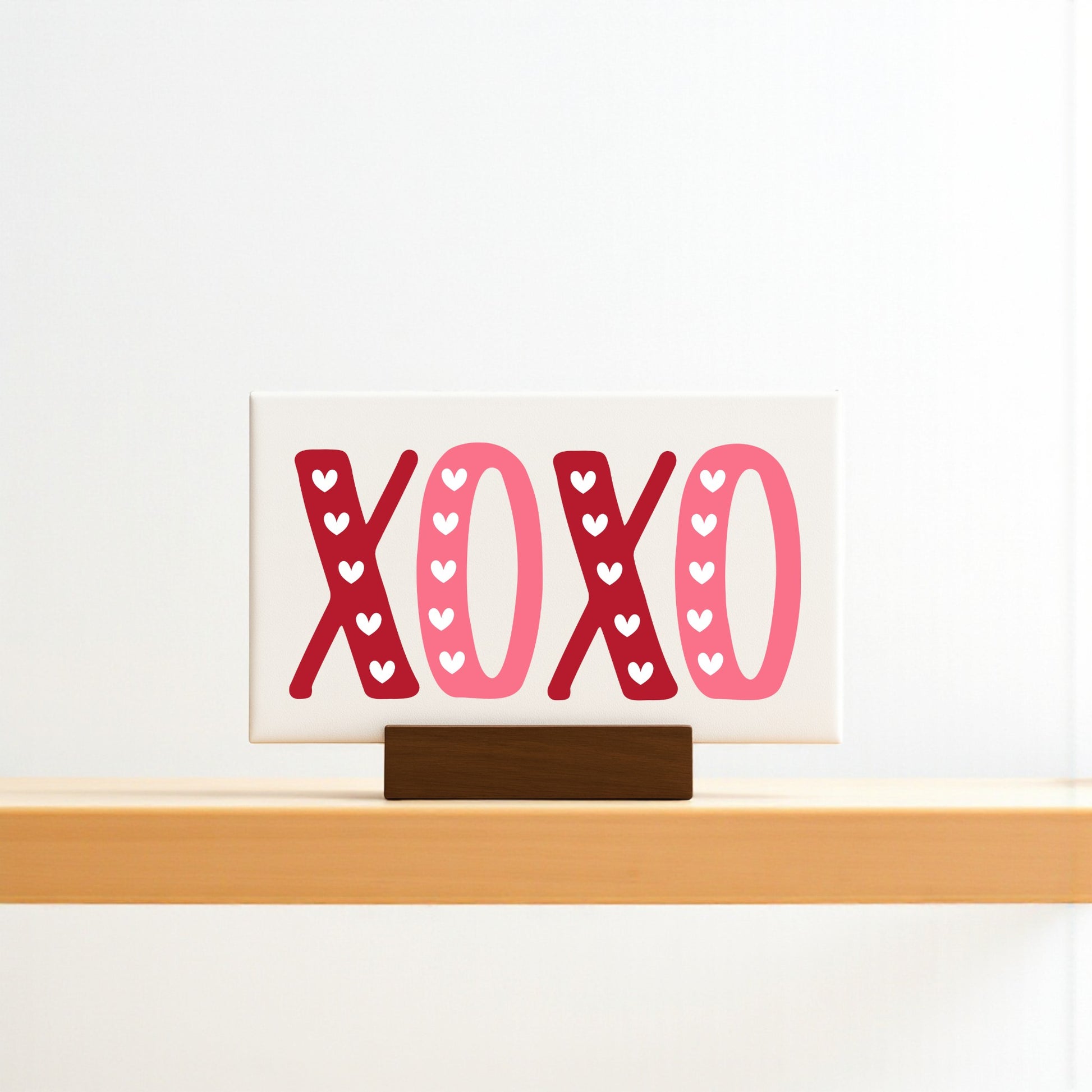 The Mirabilia Boutique XOXO Valentine's Sign is a 6x4 canvas with a wood base, featuring bold red and pink letters with tiny white hearts—ideal Valentine’s Day decor.