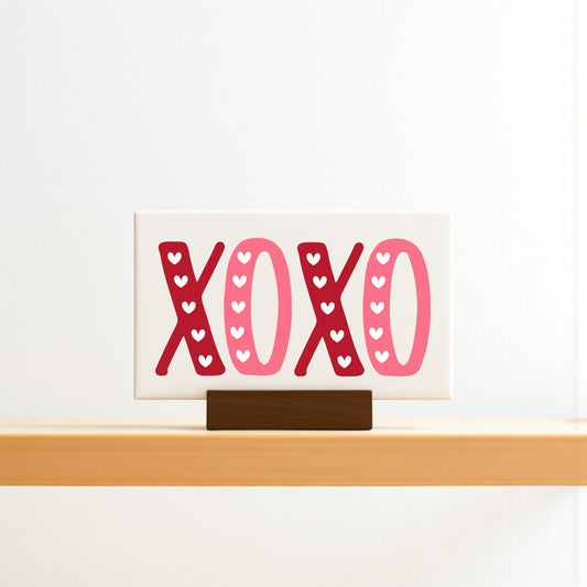 The Mirabilia Boutique XOXO Valentine's Sign is a 6x4 canvas with a wood base, featuring bold red and pink letters with tiny white hearts—ideal Valentine’s Day decor.