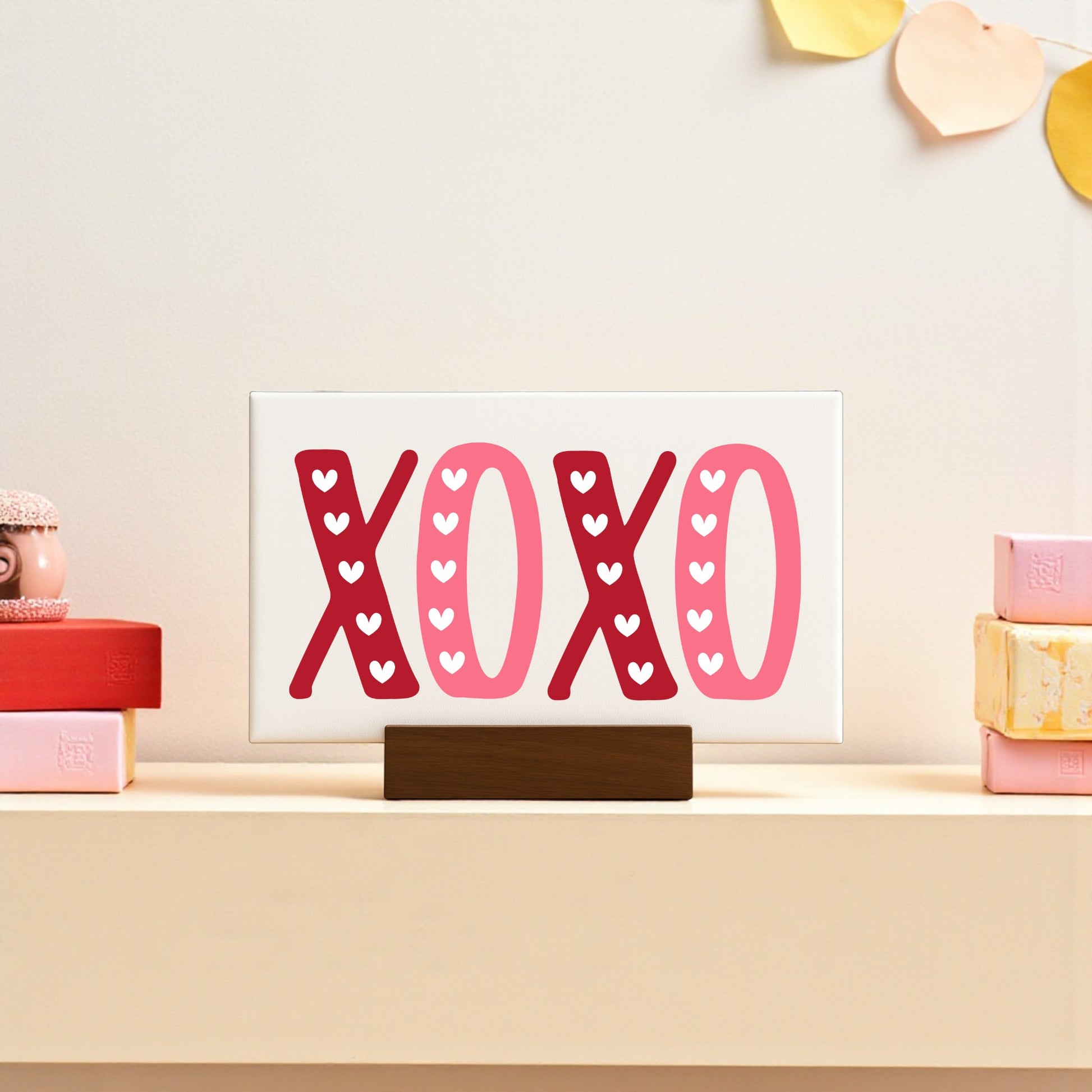 The Mirabilia Boutique XOXO Valentine's Sign, a 6x4 canvas with wood base, features red and pink hues with white hearts—perfect Valentine’s Day decor for your shelf alongside heart garlands and pastel gift boxes.