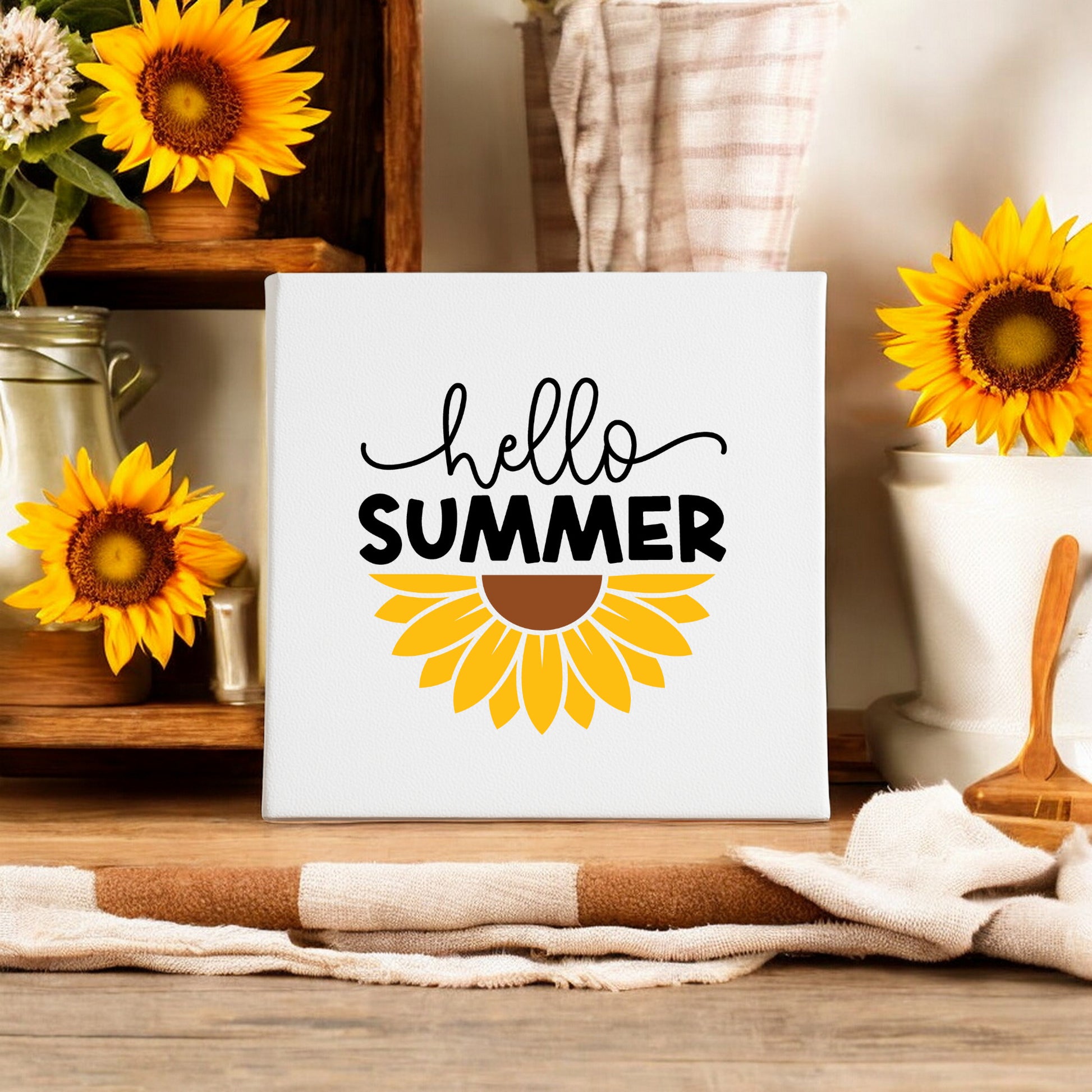 The Hello Summer Sunflower Canvas Sign – 8x8 Wall Art by Mirabilia Boutique brightens a kitchen counter, paired with farmhouse decor, jars, a wooden spoon, and a striped towel.