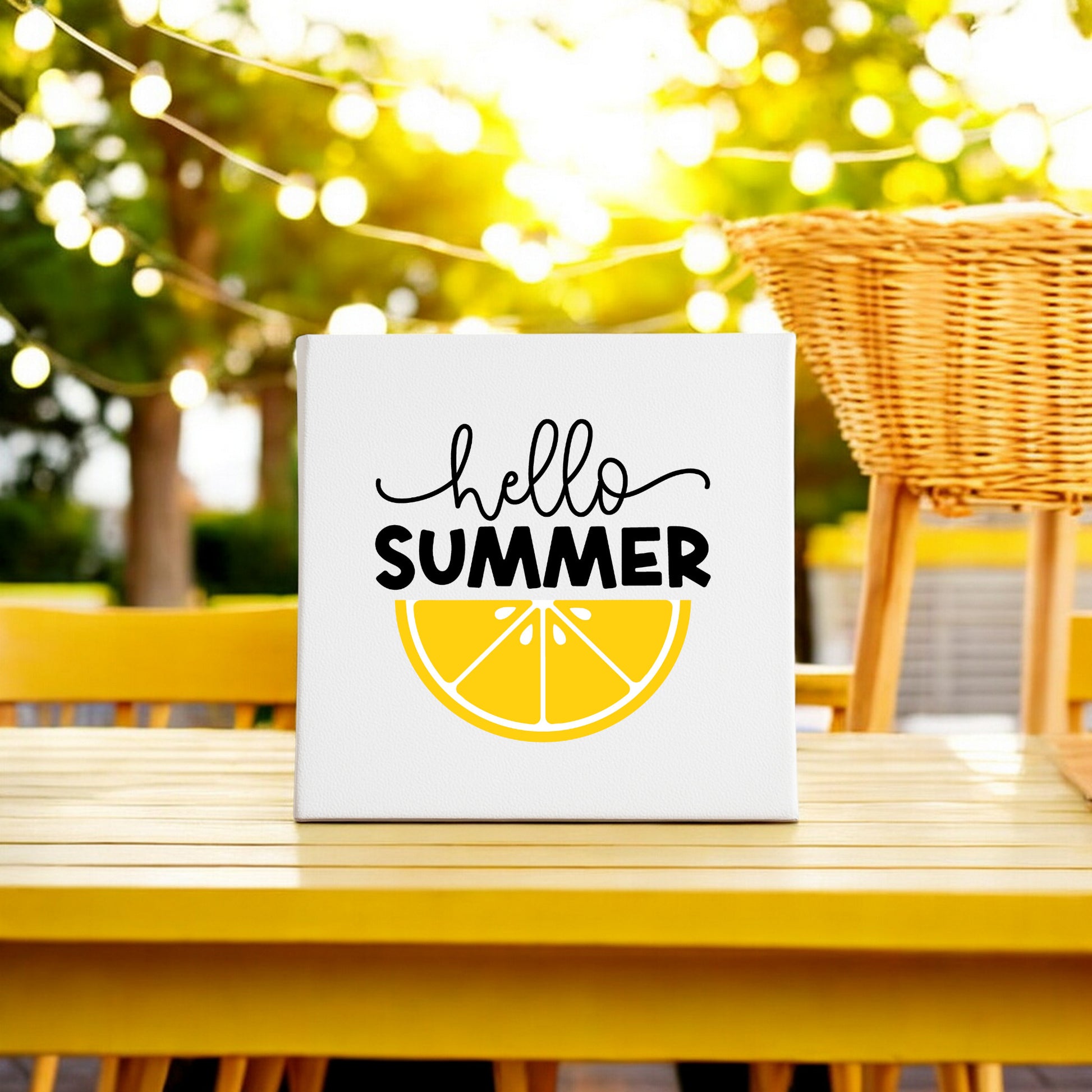 The Mirabilia Boutique Hello Summer Lemon Canvas Sign – 8x8 Wall Art adds cheerful lemon decor to a yellow outdoor table with string lights and a wicker chair under a sunny sky.