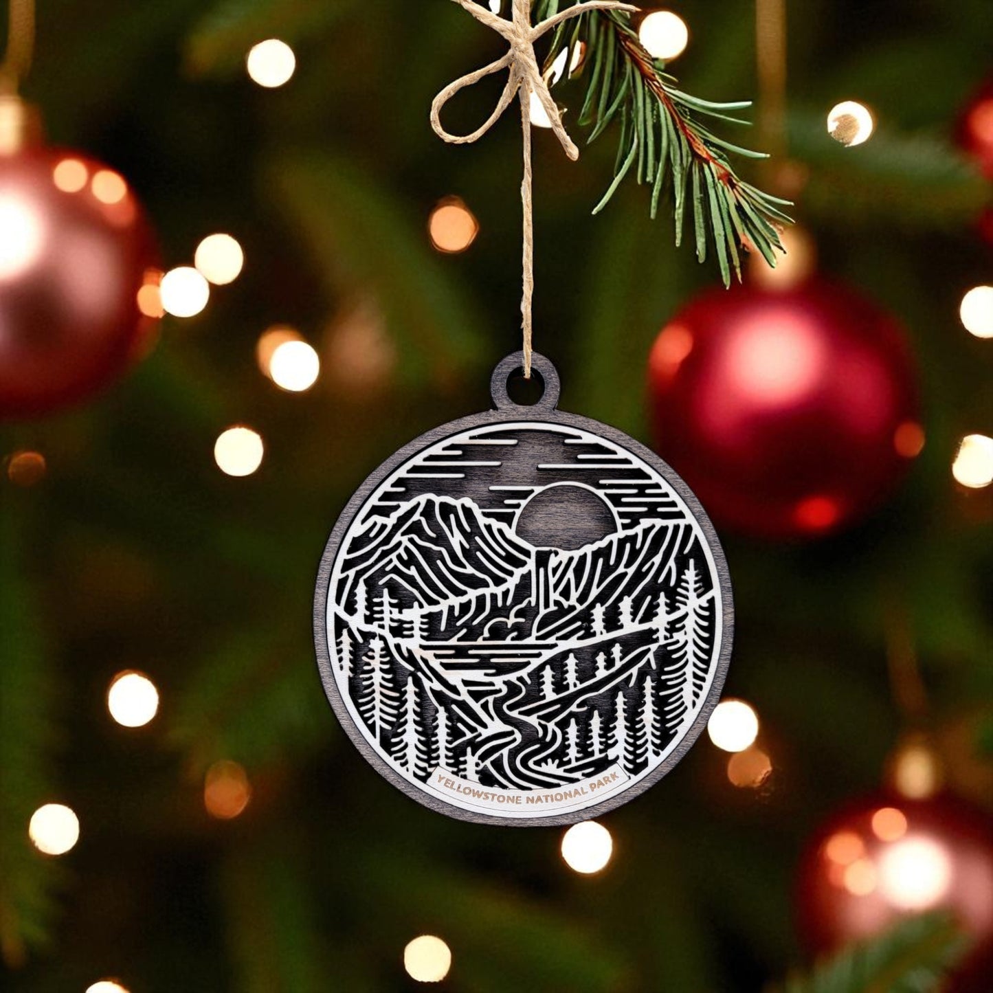 The Yellowstone National Park Ornament by Mirabilia Boutique is a handcrafted wooden decoration featuring laser-cut trees, mountains, and a river—perfect for adding rustic charm to your Christmas tree this holiday season.