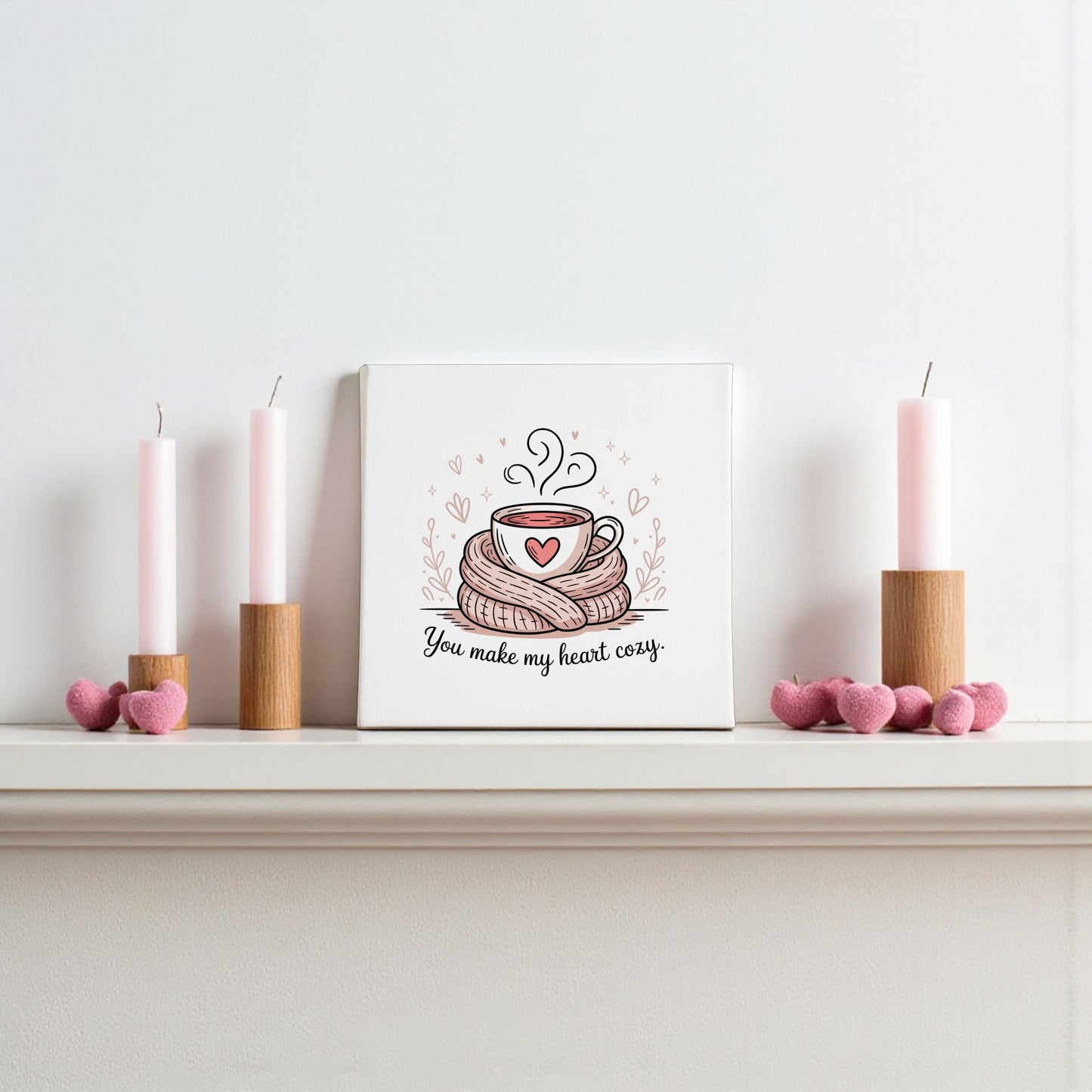 A white mantel features two pink candles in wooden holders, Mirabilia Boutique’s “You Make My Heart Cozy” canvas, and pink heart decorations—the perfect romantic gift or charming coffee decor.