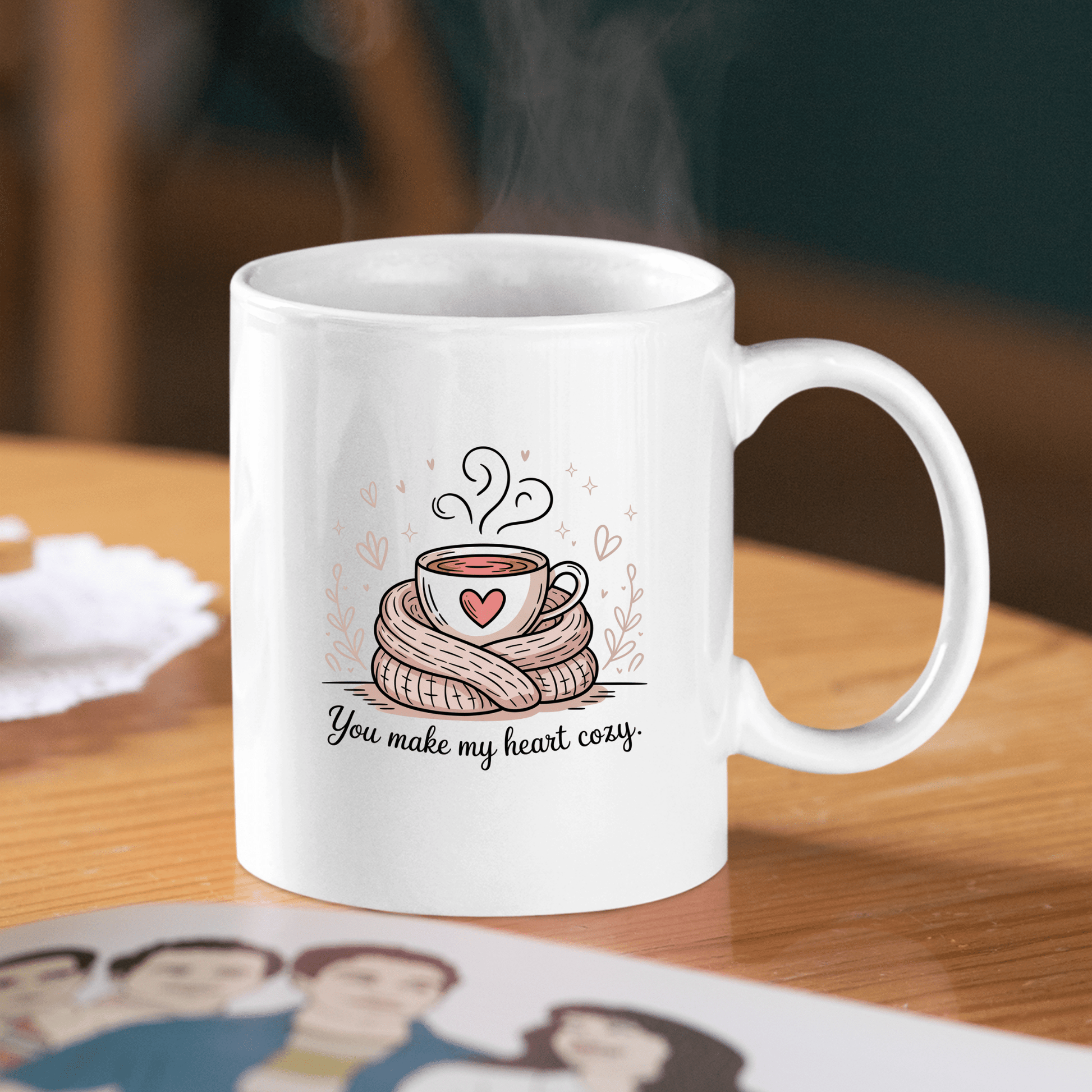 The "You Make My Heart Cozy Mug" by Mirabilia Boutique features a white design with a steaming cup in a scarf surrounded by hearts and the text "You make my heart cozy." A cute coffee lover gift, perfect for Valentine’s Day.