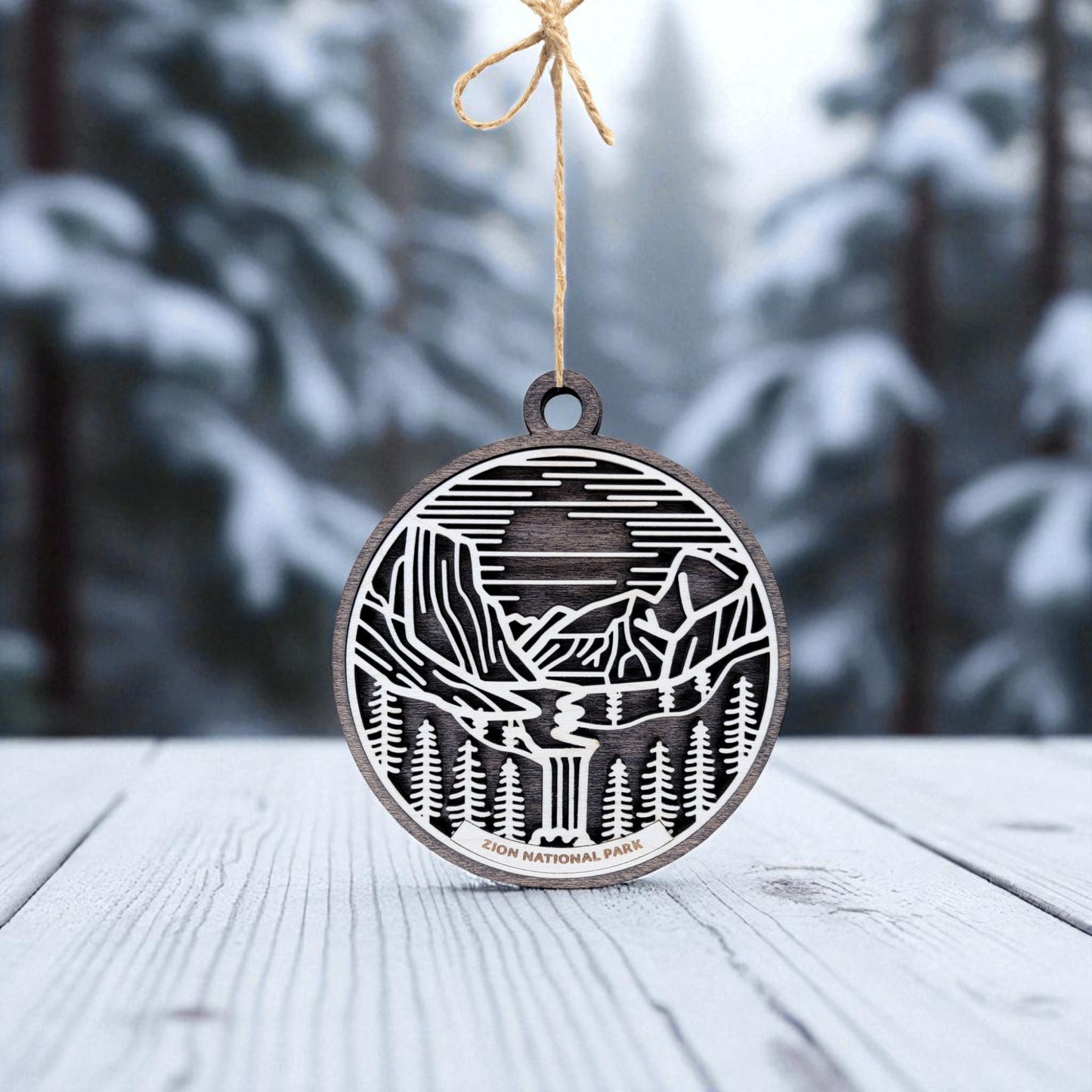 The Zion National Park Ornament by Mirabilia Boutique is a round wooden keepsake engraved with mountains, trees, and a river—perfect for nature lovers and ideal as a handcrafted gift or memento.